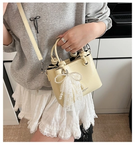 Détail du sac seau en cuir crème avec breloque perle et nœud en dentelle sur mannequin