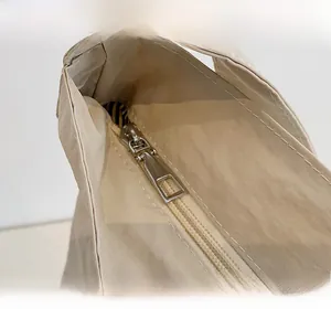 Detailed close-up of smooth silver metal zipper on light beige tote bag fabric