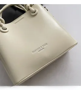 Gros plan du sac seau blanc crème avec texture cuir souple et logo embossé chic