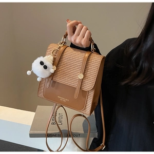 Detail view of brown woven texture handbag featuring a white faux fur pompom charm