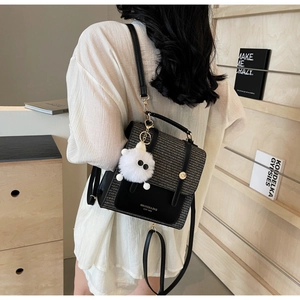 Detail of a chic two-tone woven backpack with gold buckle and plush bear charm on model