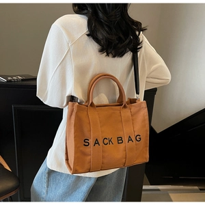 Detailed view of the brown canvas tote bag featuring Sack Bag print and black shoulder strap
