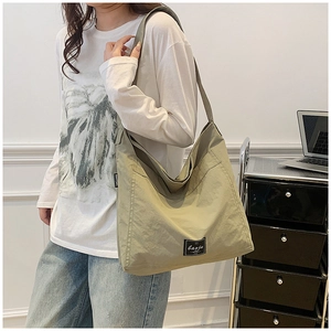 Close-up of moss green canvas tote bag with black woven label and wide shoulder strap