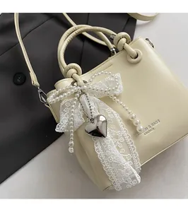Détail du sac seau crème avec nœud en dentelle, perles et pendentif cœur argenté