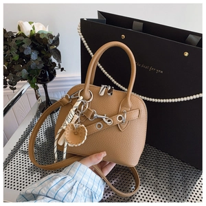Close-up of brown textured leather shell bag with striped strap and baseball glove charm