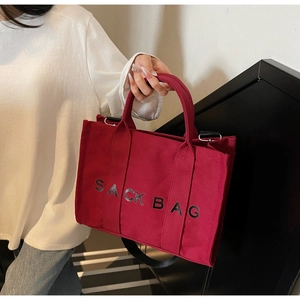 Detail of burgundy canvas sack bag with black shoulder strap shown in a daily setting