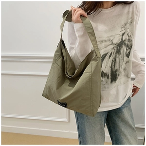 Olive green tote bag with wide shoulder strap and external pocket on a model