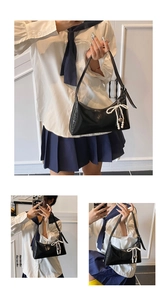 Détail d'un sac sous les bras en cuir noir avec noeud perlé et pendentif coeur en lumière douce
