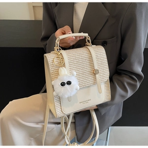 Detail of cream white bag with straw texture flap and fuzzy monster charm accessory