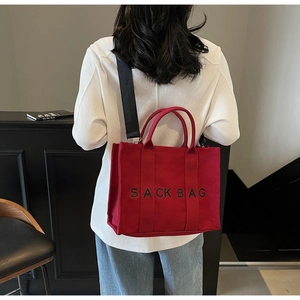 Detail view of red canvas tote bag with black SACK BAG lettering and nylon strap