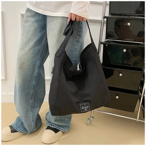 Detail showing the white woven logo label and stitching on the black nylon tote bag