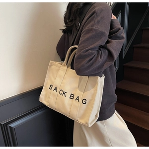Detail of off-white canvas tote bag featuring black SACK BAG print and nylon strap