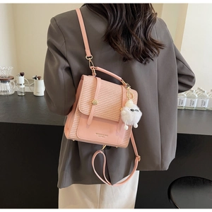 Close-up of pink woven and leather backpack with decorative white pompom charm