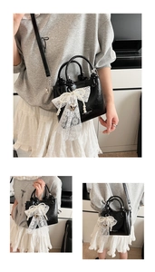 Détail du sac seau noir brillant avec nœud en dentelle blanche, perles et cœurs