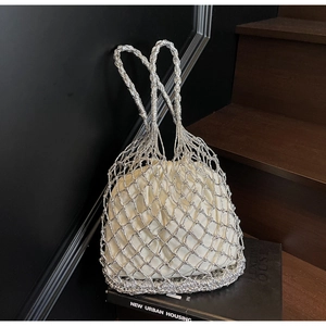 Macro shot of silver woven hollow mesh handbag with cream drawstring pouch and metallic finish