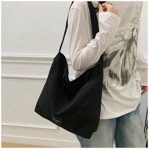 Detail view of black canvas tote bag with wide shoulder strap and white logo patch