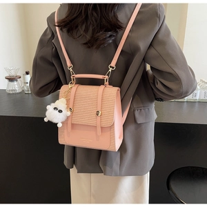 Detail view of pink leather backpack with straw woven flap and cute plush doll pendant