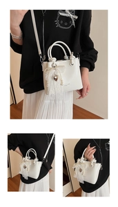 Détail du sac seau en cuir blanc avec nœud en dentelle de perles et breloque cœur