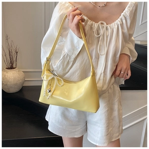 Détail macro du sac baguette en cuir jaune avec nœud en perle et pendentif cœur argenté