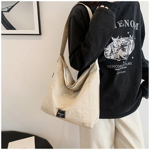 Detail view of the large beige canvas tote bag with black logo tag and hobo silhouette