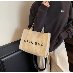 Detail view of a beige canvas tote bag with black SACK BAG text and a black shoulder strap