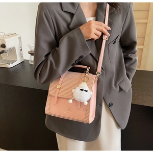Pink textured crossbody bag with woven fabric detail and cute plush charm on a grey suit jacket