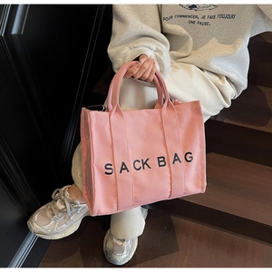 Detail of pink canvas tote bag with black SACK BAG print held by a model on stairs