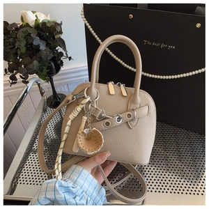 Detail of beige shell bag with lychee texture, silver hardware and a baseball charm