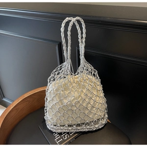 Detail of silver metal mesh tote bag with cream drawstring pouch on a black display base