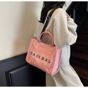 Pink canvas tote bag with Sack Bag print and black adjustable strap in casual use