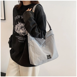 Detail of light grey large nylon tote bag with brand logo shown on person
