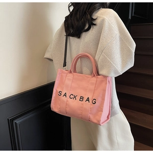 Detail of pink canvas tote bag showing thick texture, handles, and black SACK BAG print