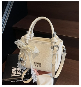 Détail du sac blanc crème avec nœud en dentelle, breloque perle et pendentif cœur argenté