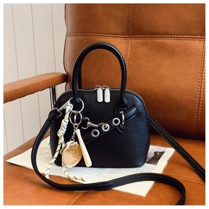 Detail of black lychee grain leather shell bag with sporty baseball charms on leather seat