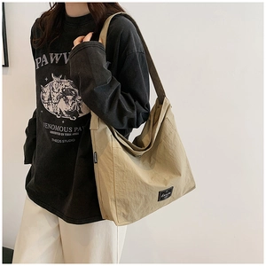 Detail of khaki canvas tote bag with brand logo label worn by a model in soft light