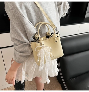 Détail du sac seau jaune crème avec pendentif nœud en dentelle perlée et anse nouée
