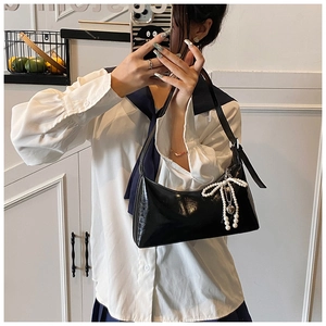 Détail du sac hobo en cuir verni noir avec nœud en perles et breloques cœur en métal