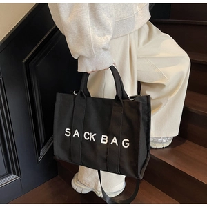 Detail of black canvas tote bag featuring SACK BAG print and metal strap buckle