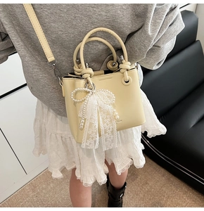 Détail du sac seau crème avec breloque nœud en dentelle perlée et finition en cuir PU lisse
