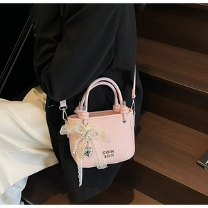 Détail du sac seau rose clair avec texture litchi, chaîne perle et logo en métal