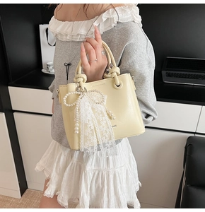 Détail du sac seau jaune crème avec nœud en dentelle perlée et lettrage BAGS