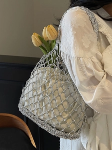 Hollow woven metallic silver mesh tote bag with a white drawstring liner and floral detail