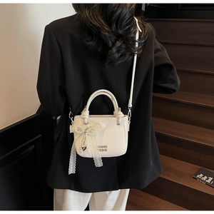 Detail of lychee textured cream bucket bag featuring lace bow and pearl charm accents