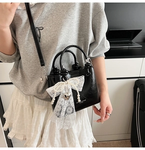 Détail du sac seau en cuir verni noir avec nœud en dentelle blanche et breloque perle