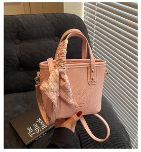 Close-up of pink litchi grain leather bucket bag with silk scarf on handle and gold logo