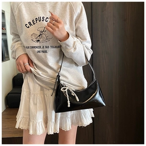 Détail du sac sous le bras en cuir verni noir avec un pendentif nœud en perles