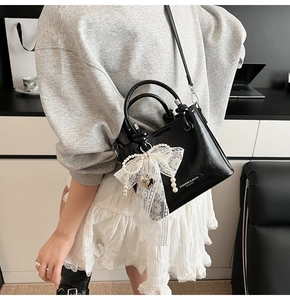 Détail du sac seau noir avec nœud en dentelle blanche, perles et breloque en cœur