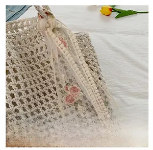 Detail of crochet straw beach bag featuring pink floral embroidery and lace ribbon