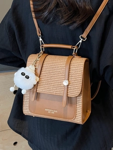 Chic brown woven leather backpack with plush pendant shown being worn on black outfit