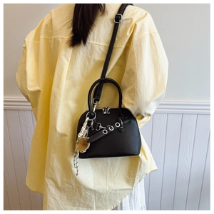 Detail of black pebbled leather shell bag with silver eyelet strap and heart charm